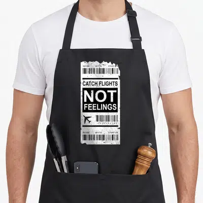 Traveler trips apron - Distressed boarding pass graphic with catch flights not feelings text and airline codes — shown on a black cotton canvas apron against a white background