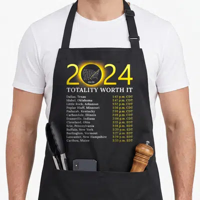 Worth eclipse apron - 2024 Totality Worth It text with US map and city times in yellow and white — shown on a black cotton canvas apron against a white background