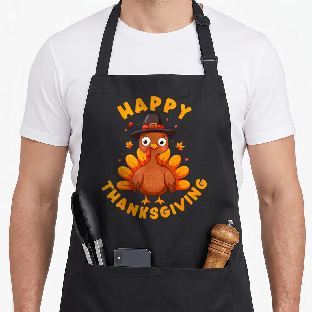 Family dinner thanksgiving day aprons - Cartoon turkey in pilgrim hat with arched HAPPY THANKSGIVING text and orange — shown on a black cotton canvas apron against a white background