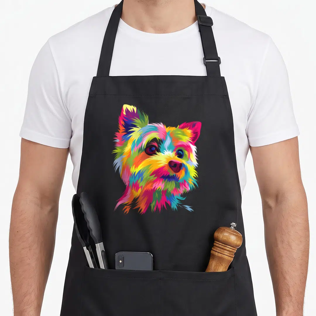 Colorful yorkie apron - Multicolored cartoon Yorkshire Terrier head in pink, yellow, blue, green, and orange pop art — shown on a black cotton canvas apron against a white background