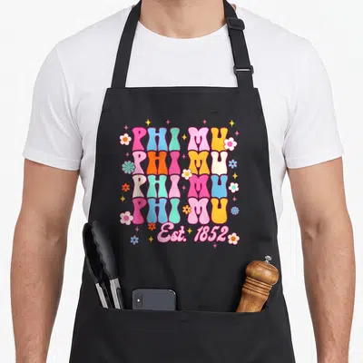 Phi mu aprons - Retro stacked PHI MU text with flowers and stars in pink blue yellow and orange — shown on a black cotton canvas apron against a white background