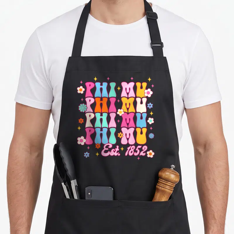 Phi mu aprons - Retro stacked PHI MU text with flowers and stars in pink blue yellow and orange — shown on a black cotton canvas apron against a white background