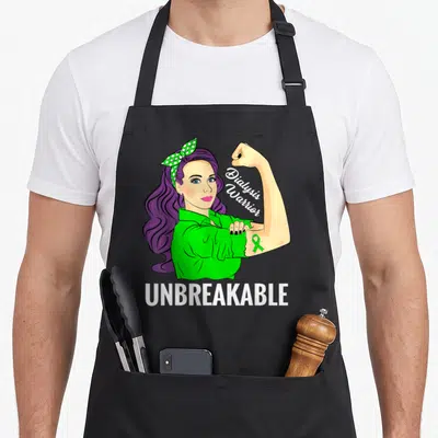 Dialysis crew apron - Cartoon woman with purple hair flexing arm showing green ribbon and text Dialysis Warrior — shown on a black cotton canvas apron against a white background