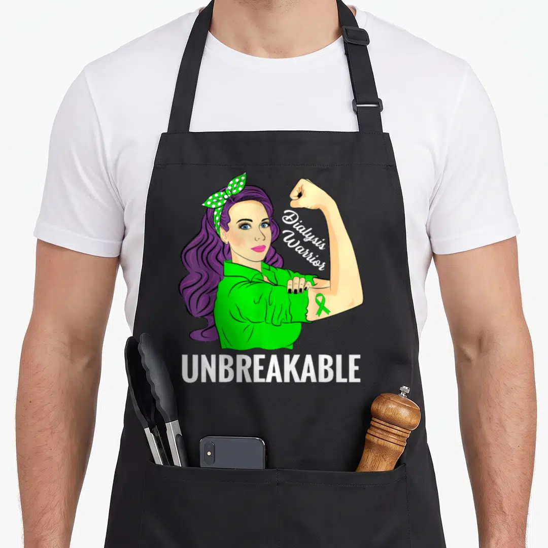 Dialysis crew apron - Cartoon woman with purple hair flexing arm showing green ribbon and text Dialysis Warrior — shown on a black cotton canvas apron against a white background