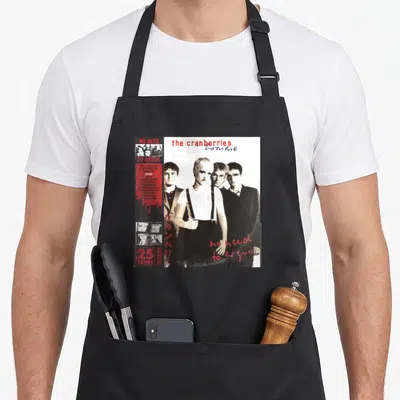 Argue blackberries apron - Cranberries band photo collage with tracklist, Japanese text, and 25 years logo in white — shown on a black cotton canvas apron against a white background