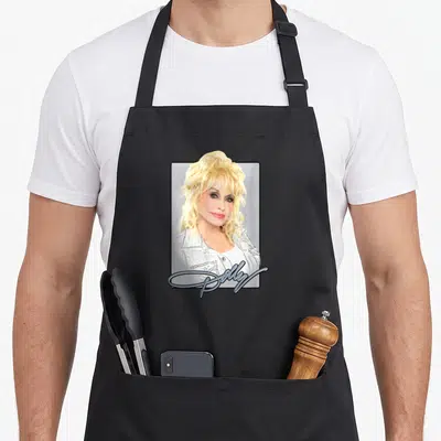 Funny dolly parton apron - Framed photo of blonde Dolly Parton with script text Dolly at bottom — shown on a black cotton canvas apron against a white background