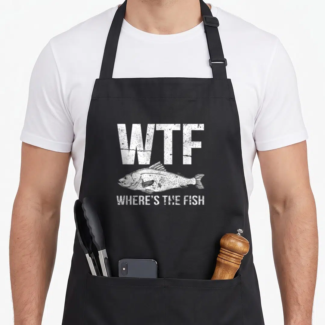 Cute fish apron - WTF Where's The Fish white distressed text above a fish sketch — shown on a black cotton canvas apron against a white background