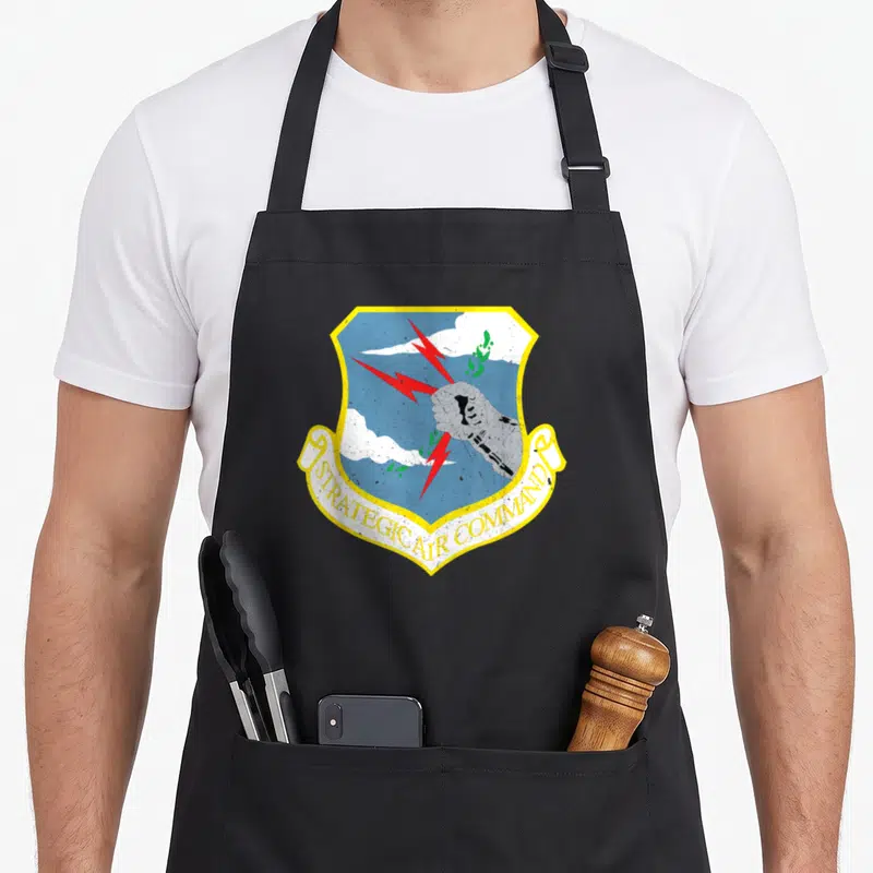 Strategic cold war era apron - Strategic Air Command shield with fist, lightning bolts, and clouds in blue yellow red — shown on a black cotton canvas apron against a white background