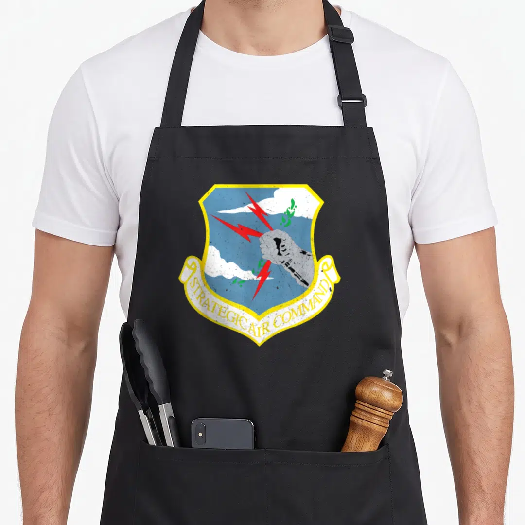 Strategic cold war era apron - Strategic Air Command shield with fist, lightning bolts, and clouds in blue yellow red — shown on a black cotton canvas apron against a white background