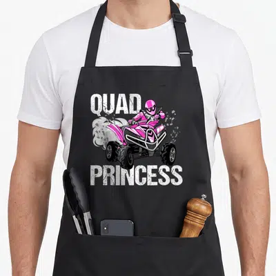 Quad princess apron - Pink ATV rider with white QUAD PRINCESS text and smoke clouds — shown on a black cotton canvas apron against a white background
