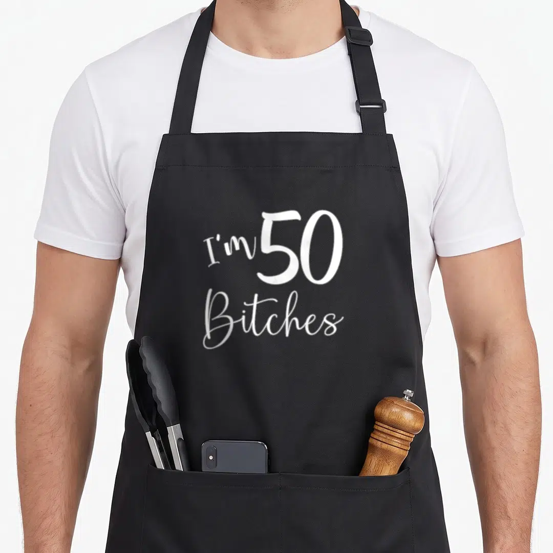 50th age birthday apron - White I'm 50 Bitches script typography on black background — shown on a black cotton canvas apron against a white background