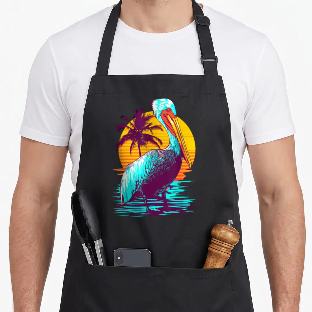 Bird animal print apron - Retro pelican standing on cyan water in front of yellow sun and purple palm tree — shown on a black cotton canvas apron against a white background