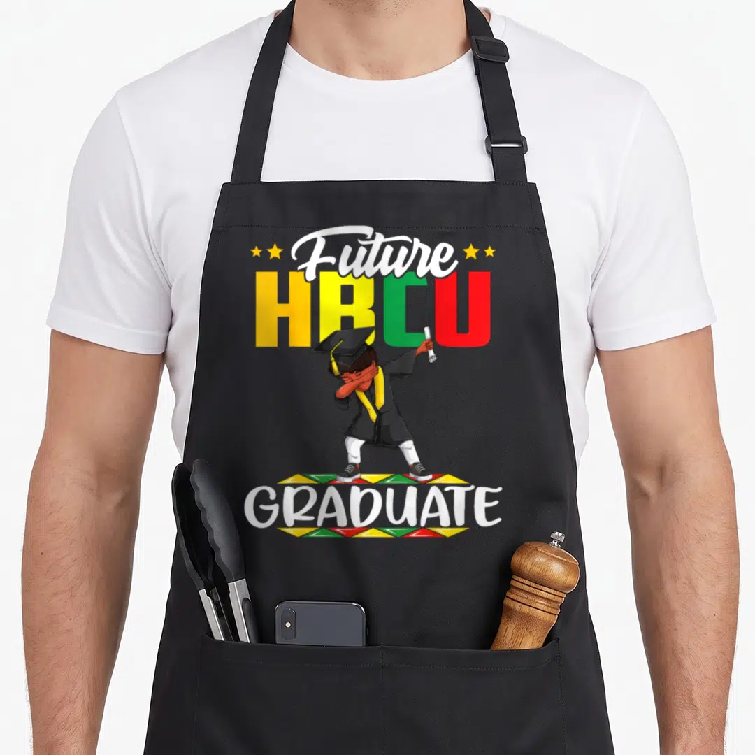 Future college apron - Cartoon graduate boy dabbing in front of Future HBCU GRADUATE text with geometric border — shown on a black cotton canvas apron against a white background