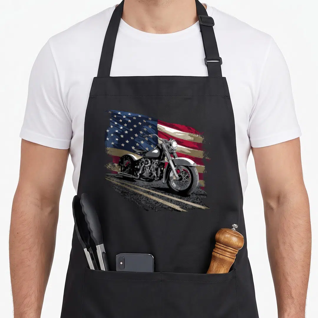 Open american flag apron - Realistic motorcycle on road with waving red white blue flag background — shown on a black cotton canvas apron against a white background