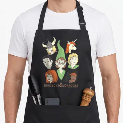 Shot cartoon apron - Six fantasy heads and DUNGEONS & DRAGONS text on grey background — shown on a black cotton canvas apron against a white background