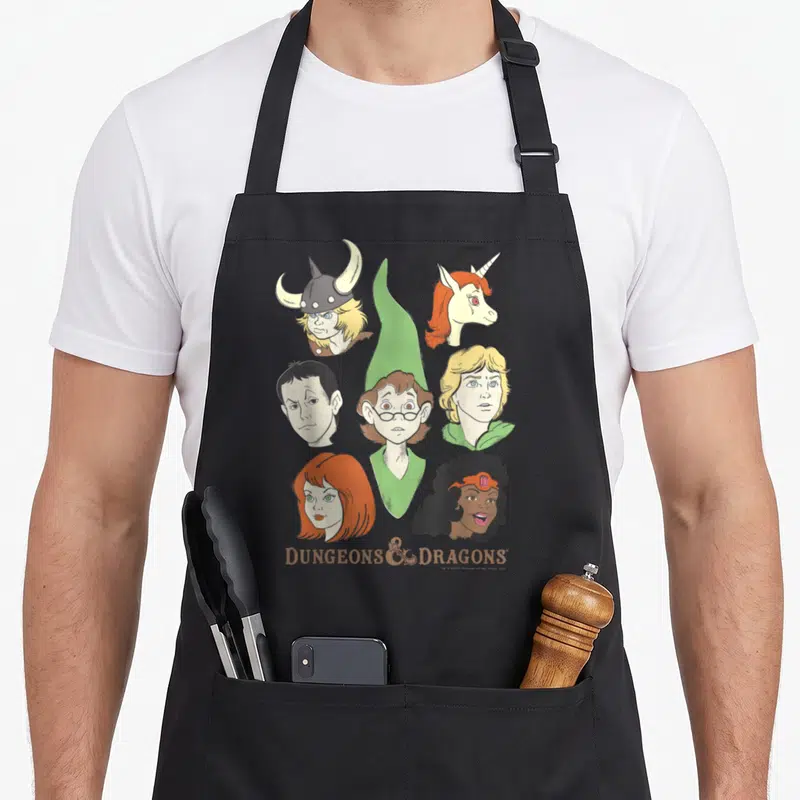 Shot cartoon apron - Six fantasy heads and DUNGEONS & DRAGONS text on grey background — shown on a black cotton canvas apron against a white background