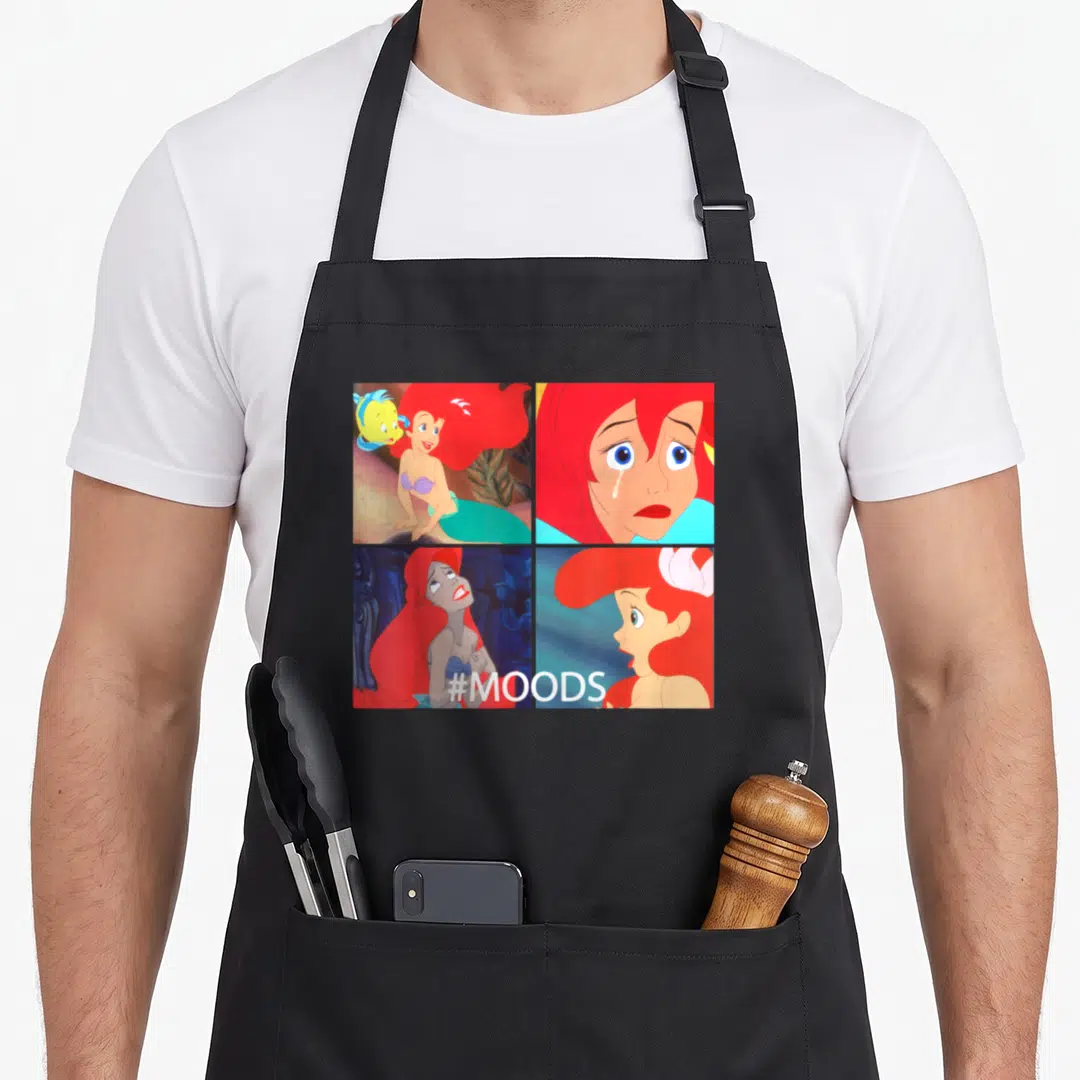 Mood mermaid apron - Four panel grid of Ariel expressions with #MOODS text in red blue teal and yellow — shown on a black cotton canvas apron against a white background