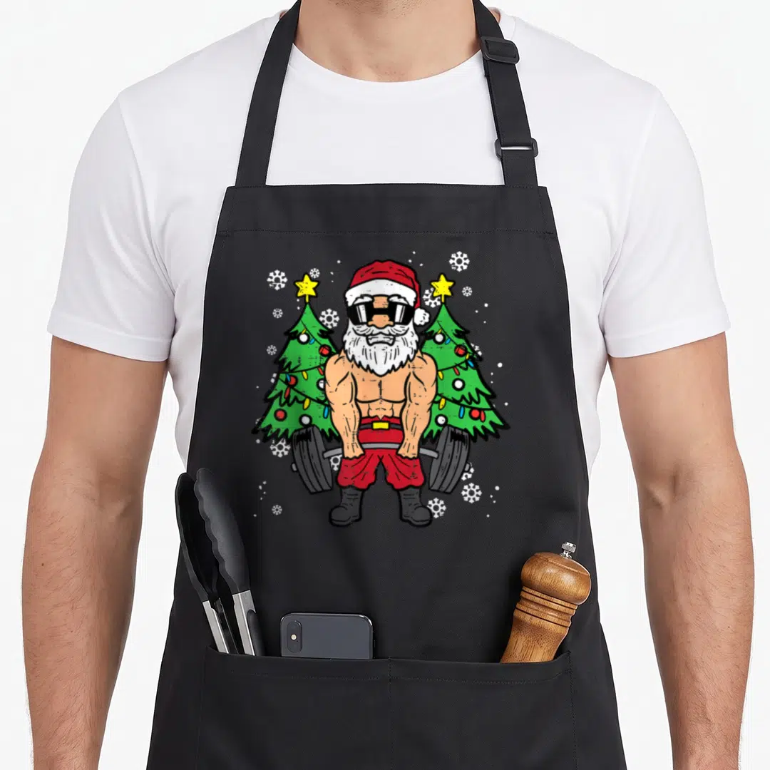 Deadlift christmas santa apron - Cartoon Santa lifting a barbell between two Christmas trees with snowflakes — shown on a black cotton canvas apron against a white background