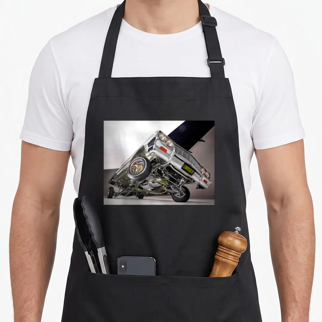 Funny lowrider car apron - Silver lowrider car tilted on hydraulics with gold wheels and LOWRIDER license plate — shown on a black cotton canvas apron against a white background