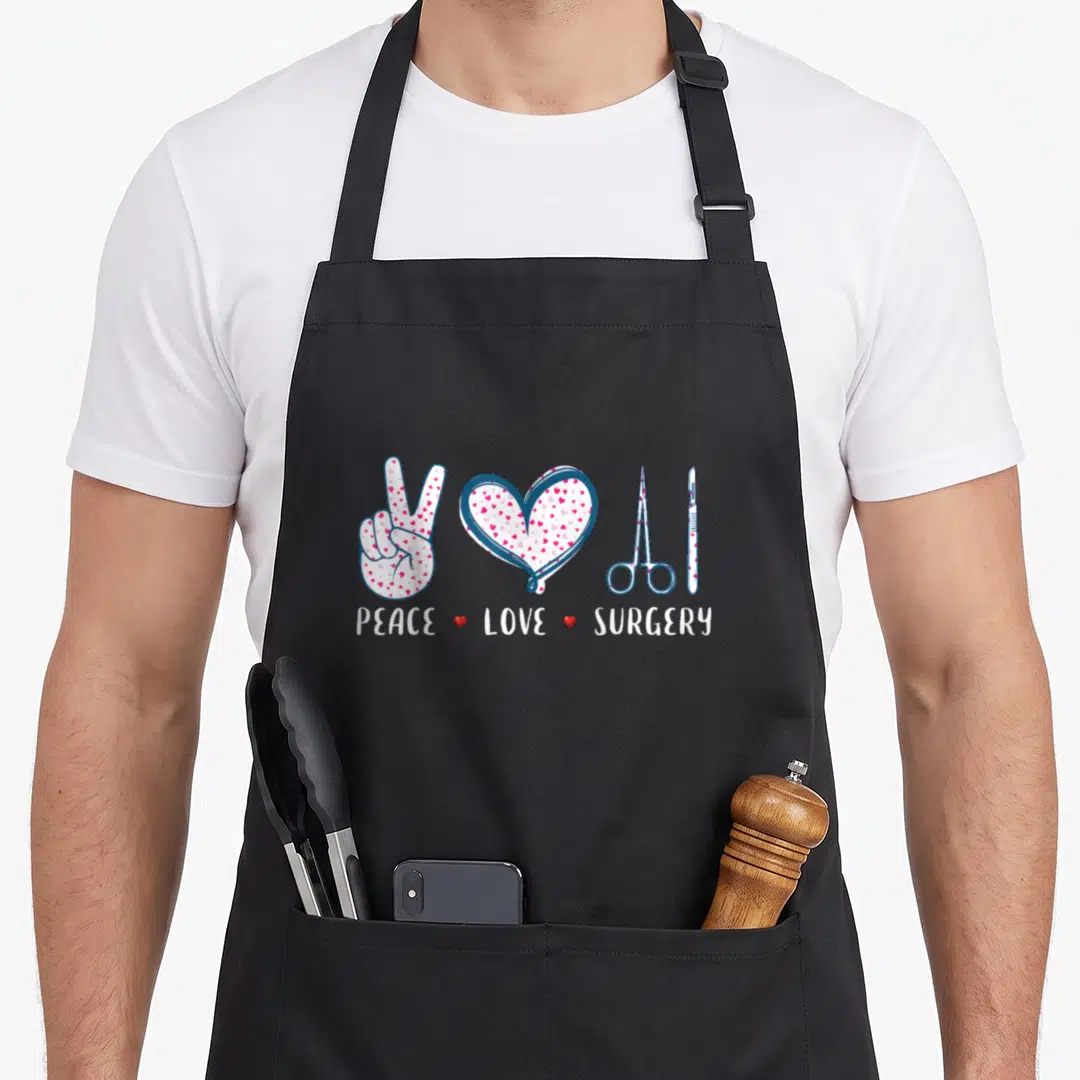 Peace surgeon apron - PEACE LOVE SURGERY text below hand heart scissors scalpel in blue pink red — shown on a black cotton canvas apron against a white background