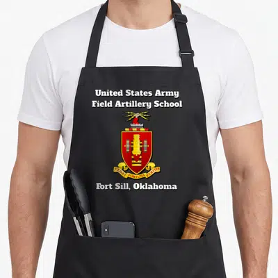Artillery field apron - Red gold and black Field Artillery School crest with lightning bolt and cannon shield on black — shown on a black cotton canvas apron against a white background