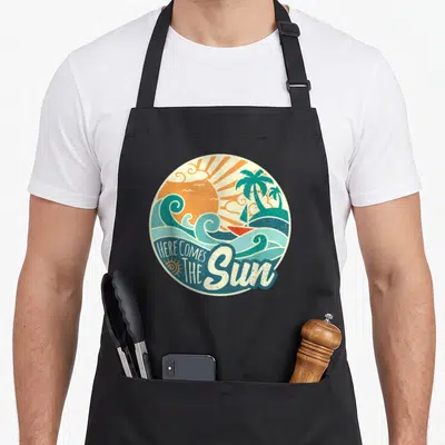 Summer come and get it apron - Retro circular print with orange sun, teal palms, waves, sailboat, and HERE COMES — shown on a black cotton canvas apron against a white background