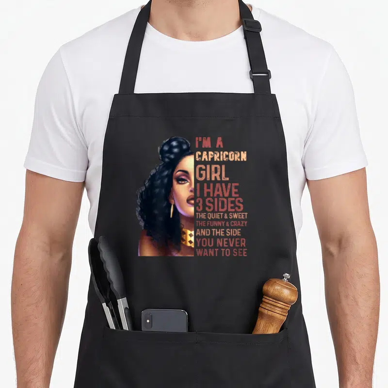 Capricorn astrology zodiac aprons - Realistic woman portrait with stacked text about Capricorn girl having three sides — shown on a black cotton canvas apron against a white background