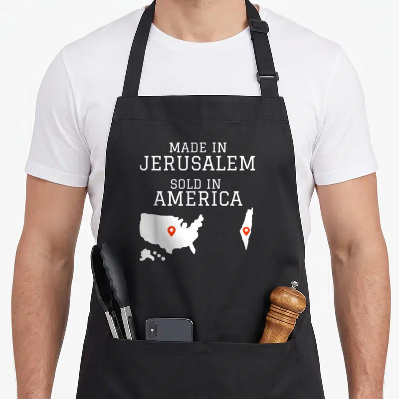 Jerusalem hebrew aprons - White text MADE IN JERUSALEM SOLD IN AMERICA above USA and Israel maps with red pins — shown on a black cotton canvas apron against a white background