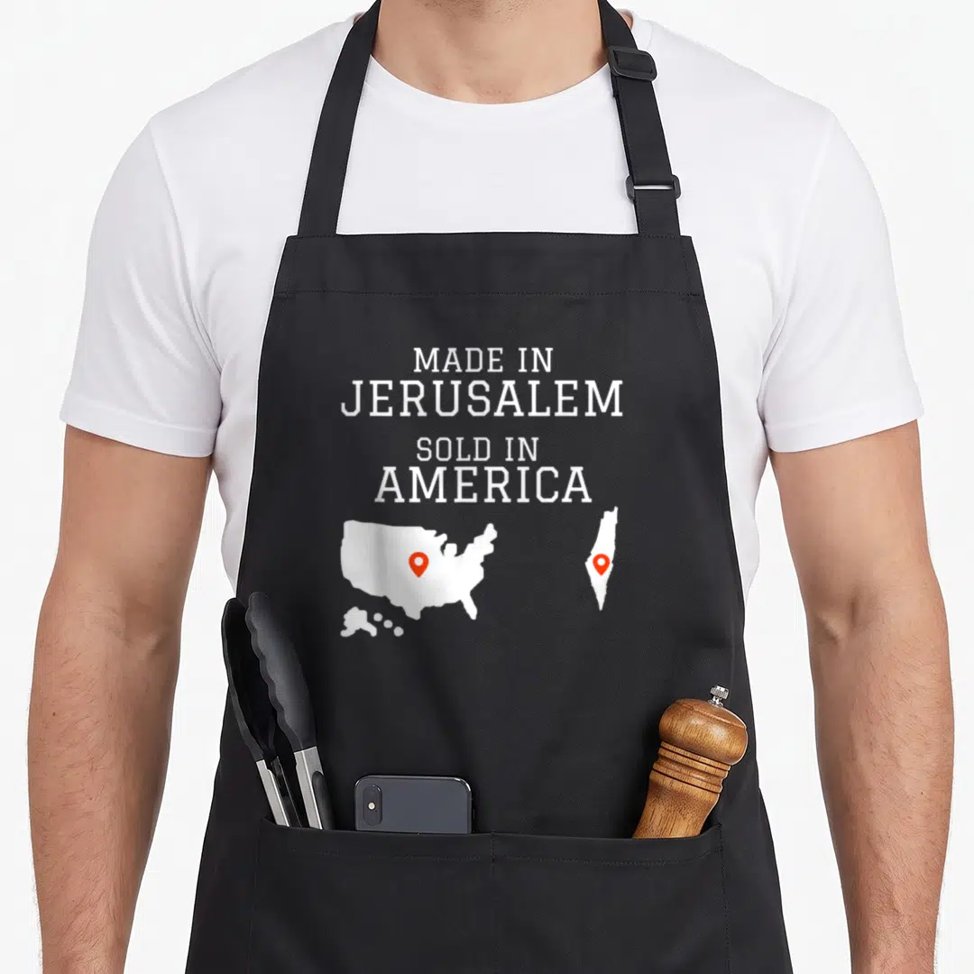 Jerusalem hebrew aprons - White text MADE IN JERUSALEM SOLD IN AMERICA above USA and Israel maps with red pins — shown on a black cotton canvas apron against a white background