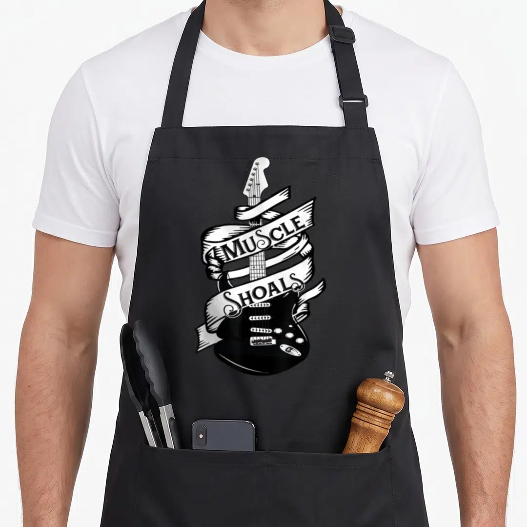 Music alabama apron - Black electric guitar wrapped in white ribbon with Muscle Shoals text in line art style — shown on a black cotton canvas apron against a white background
