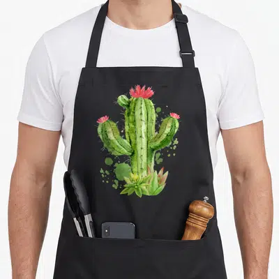 Blooming flower cactus apron - Watercolor green cactus with pink flowers and succulents at base — shown on a black cotton canvas apron against a white background