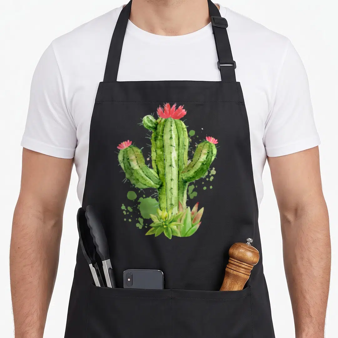 Blooming flower cactus apron - Watercolor green cactus with pink flowers and succulents at base — shown on a black cotton canvas apron against a white background