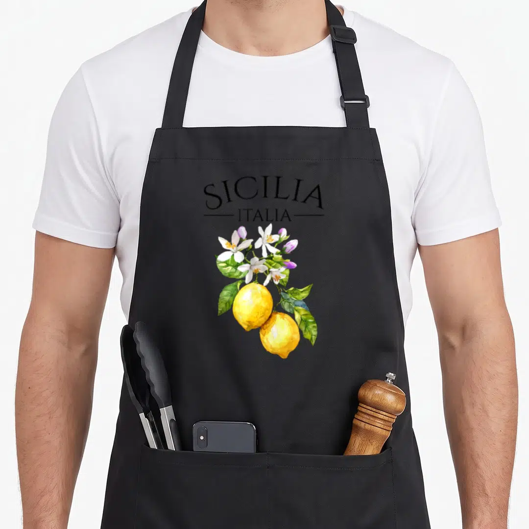 Sicilia lemon apron - Watercolor yellow lemons and white blossoms below black Sicilia Italia text — shown on a black cotton canvas apron against a white background