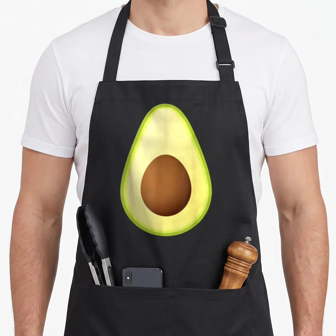 Costume avocado apron - Minimalist avocado cross-section in green, yellow, and brown centered on fabric — shown on a black cotton canvas apron against a white background