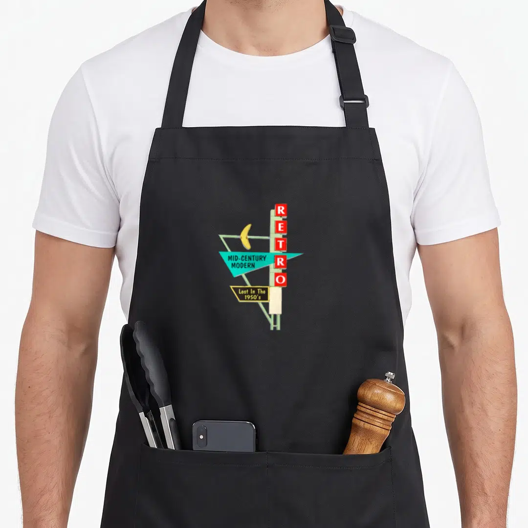 Funny mid modern apron - Vertical sign with red RETRO blocks, teal MID-CENTURY MODERN triangle, and yellow 1950s — shown on a black cotton canvas apron against a white background