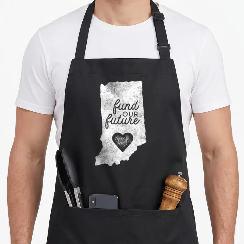 Fund teacher apron - Distressed white Indiana map shape with fund OUR future text and grey heart — shown on a black cotton canvas apron against a white background