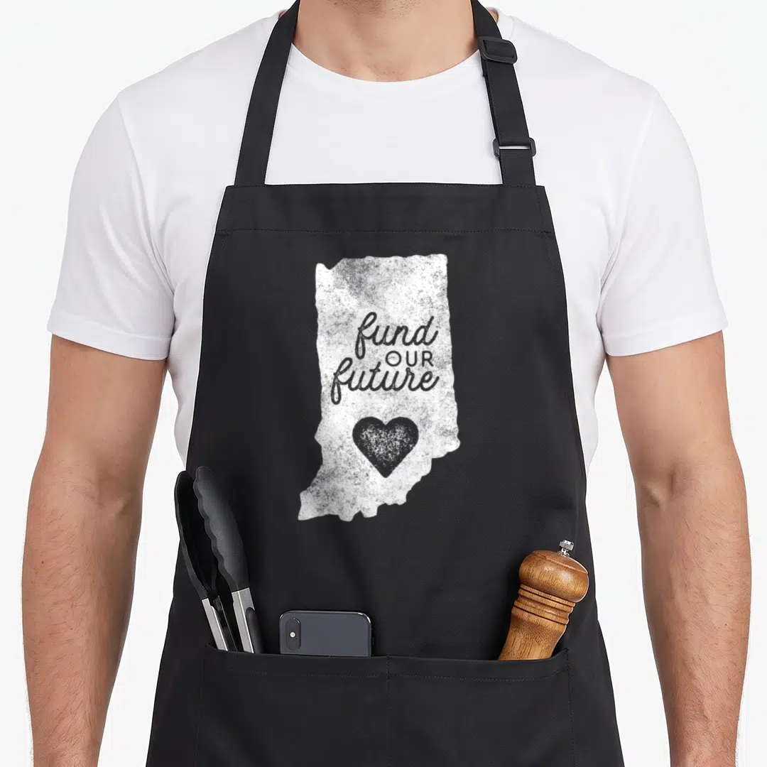 Fund teacher apron - Distressed white Indiana map shape with fund OUR future text and grey heart — shown on a black cotton canvas apron against a white background