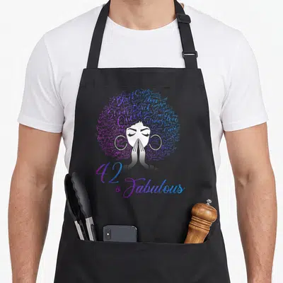 42nd hair apron - Woman silhouette with word-art afro hair in purple blue white and 42 & Fabulous text — shown on a black cotton canvas apron against a white background