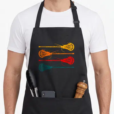 Cute lacrosse apron - Four lacrosse sticks in yellow, orange, red, and teal arranged vertically — shown on a black cotton canvas apron against a white background