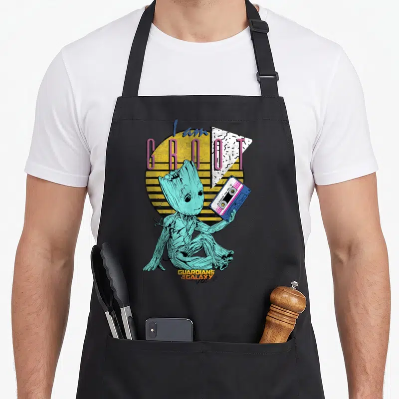 Guardian 90s apron - Teal Groot holding blue cassette tape with I am GROOT AWESOME MIX vol 2 text — shown on a black cotton canvas apron against a white background