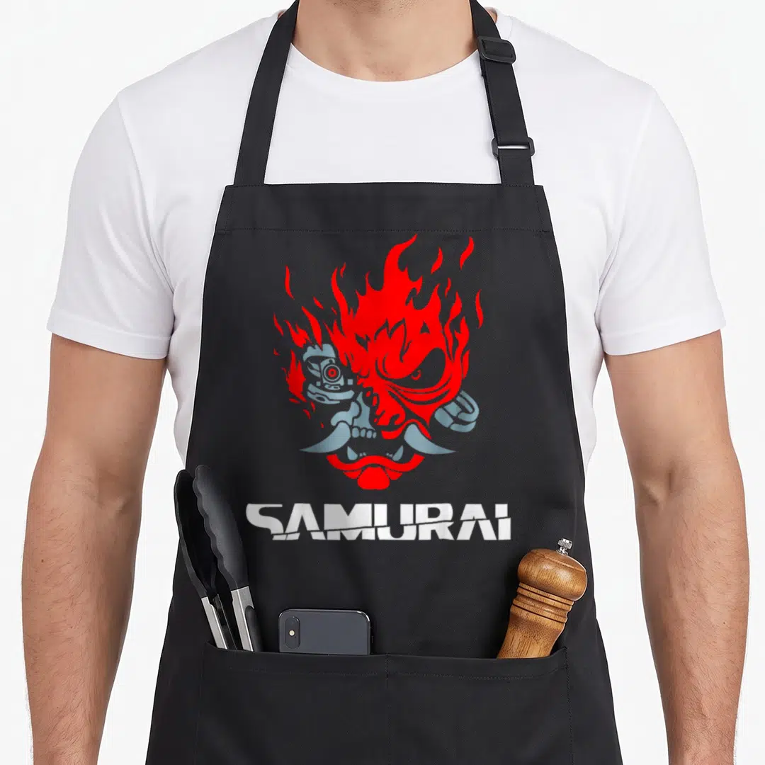 Samurai anime graphic apron - Stylized red and silver oni mask with flames and SAMURAI text below — shown on a black cotton canvas apron against a white background