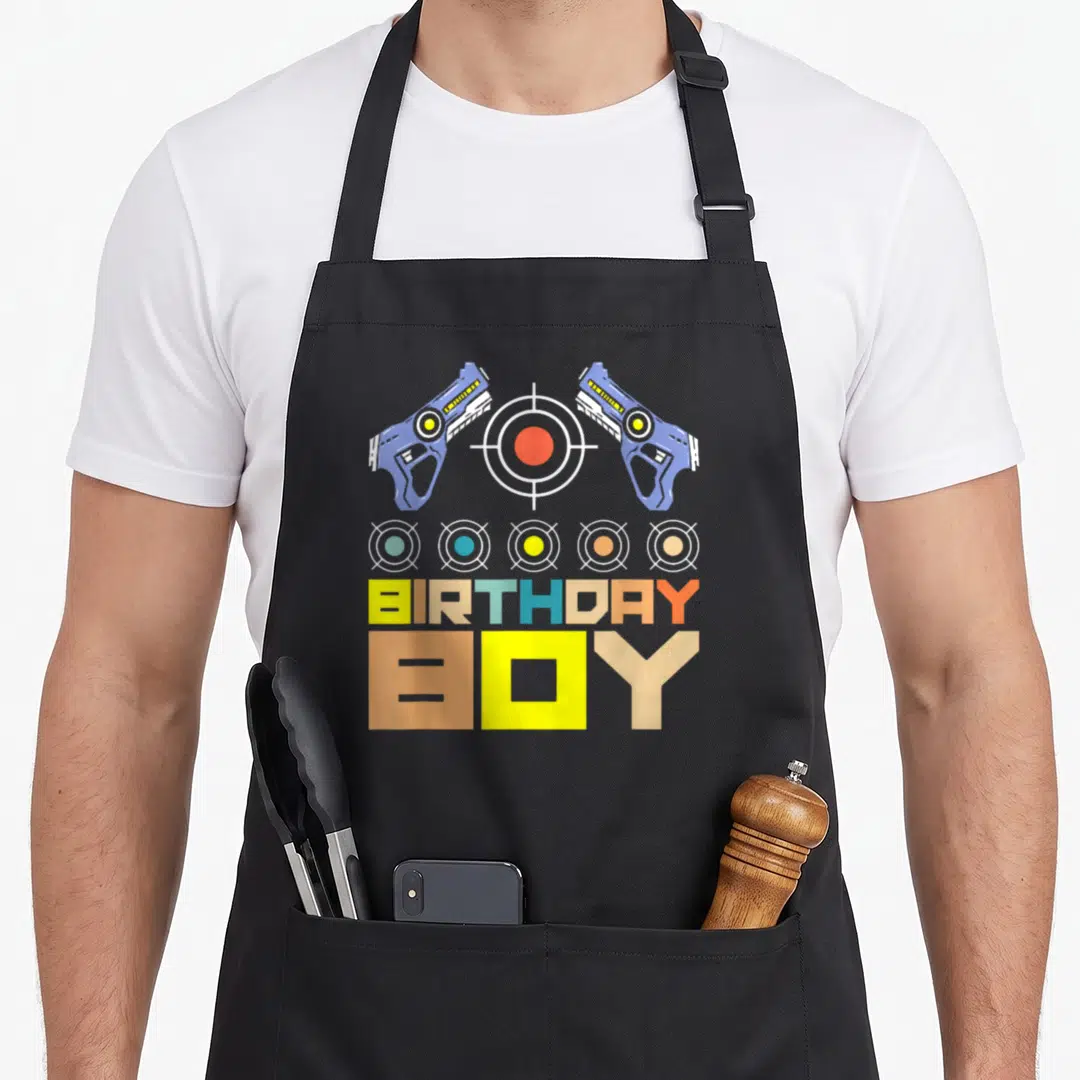 Laser birthday apron - Two blue laser guns flanking a red target above five small targets and BIRTHDAY BOY text — shown on a black cotton canvas apron against a white background