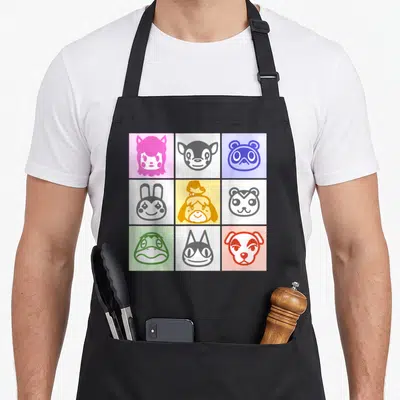 Icon animal apron - Nine cartoon animal faces in a 3x3 grid of pink, grey, blue, yellow, green, and red squares — shown on a black cotton canvas apron against a white background