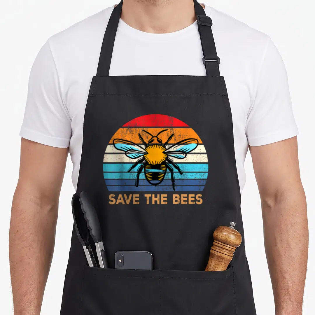 Save bee change apron - Retro bee illustration on striped semi-circle with SAVE THE BEES text below — shown on a black cotton canvas apron against a white background