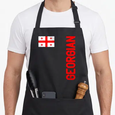 Root georgian apron - Red and white Georgian flag next to vertical red GEORGIAN text — shown on a black cotton canvas apron against a white background