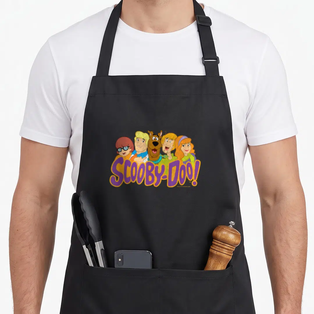 Gang decade apron - Scooby-Doo gang peering over purple SCOOBY-DOO! text — shown on a black cotton canvas apron against a white background