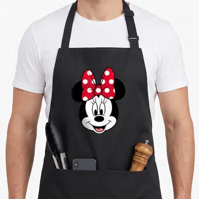 Funny face pretty apron - Cartoon mouse head with red bow and white polka dots on black background — shown on a black cotton canvas apron against a white background