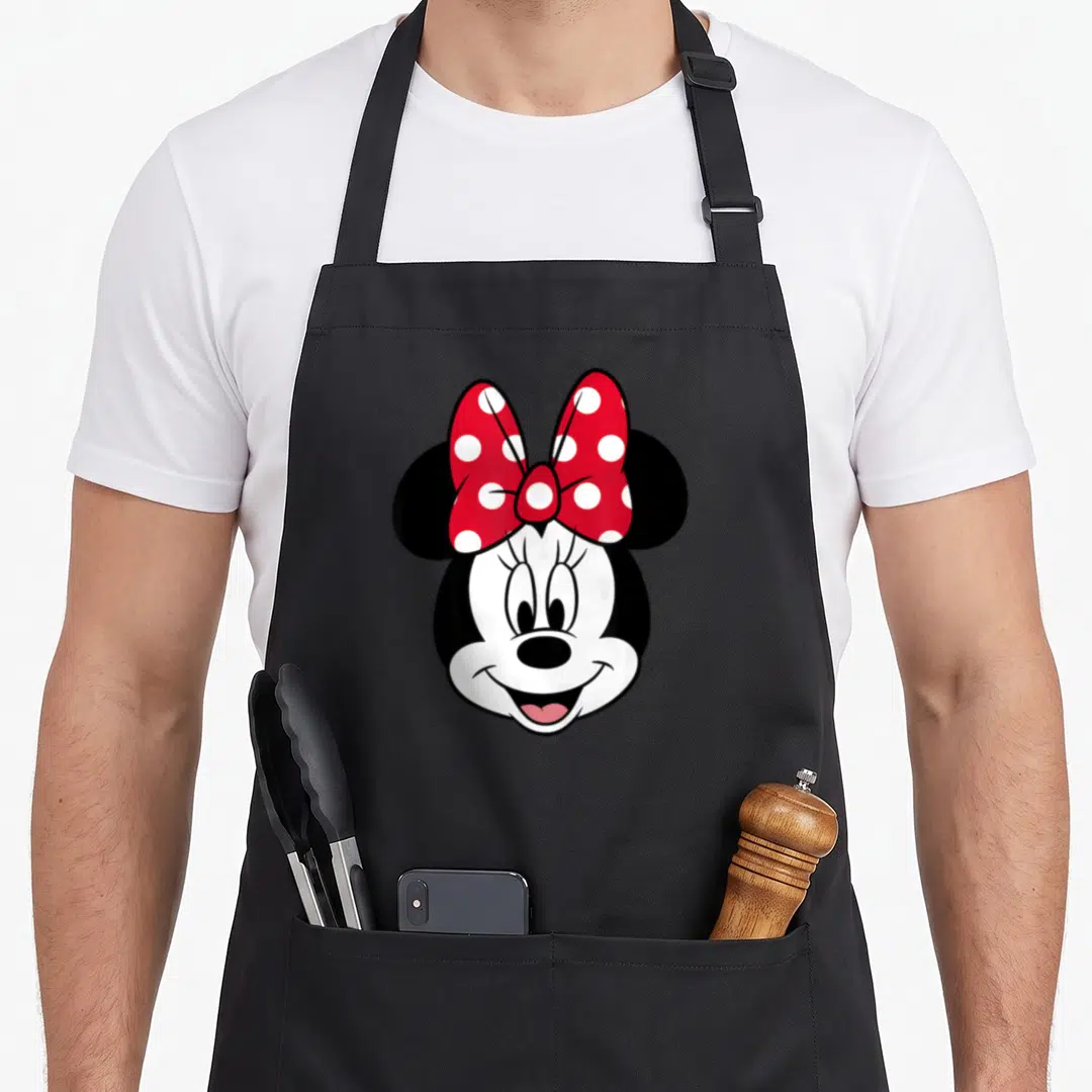 Funny face pretty apron - Cartoon mouse head with red bow and white polka dots on black background — shown on a black cotton canvas apron against a white background