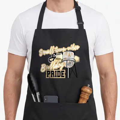 Bulldog school pride apron - Rusted water tower with bulldog logo and small town vibes text in gold and black — shown on a black cotton canvas apron against a white background