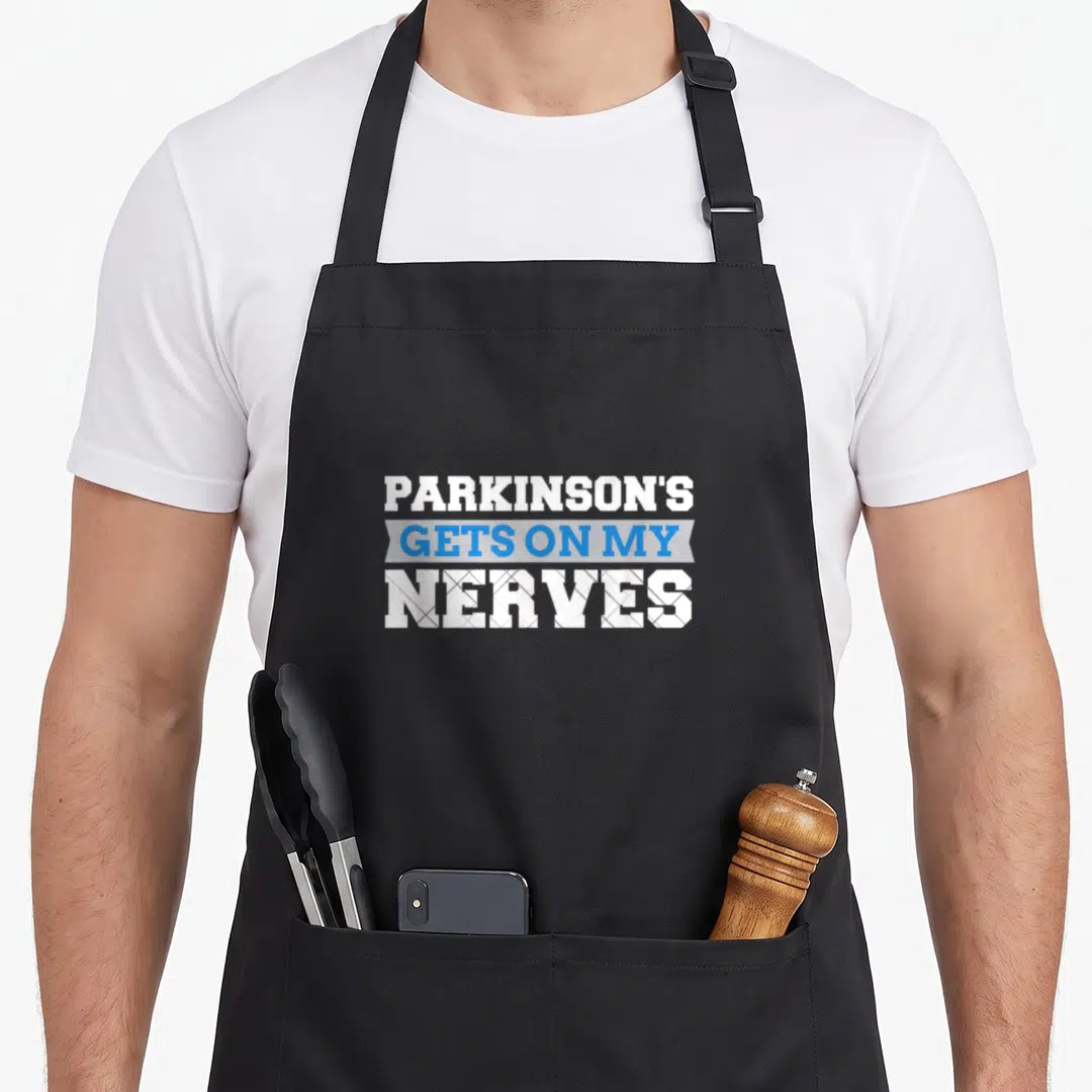 Parkinson caregiver awareness apron - PARKINSON'S GETS ON MY NERVES text in white and blue stacked layout with ribbon — shown on a black cotton canvas apron against a white background